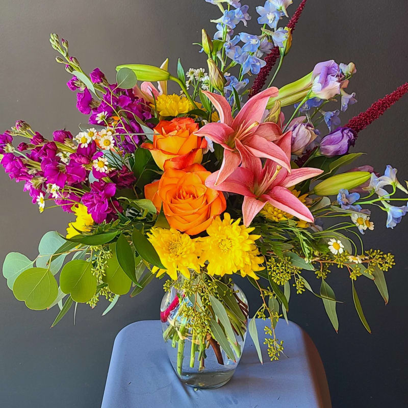 Mixed bouquet of orange roses, pink lilies, and purple flowers in a glass vase